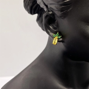 Close-up of gold pineapple stud earrings with yellow and green crystals on a black bust