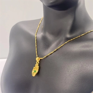 Gros plan du collier pendentif main de Hamsa doré avec pierre verte sur buste noir