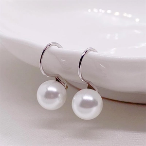 Macro shot of elegant white pearl drop earrings hanging on a white ceramic plate