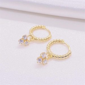 Elegant gold twisted hoop earrings with triple zircon stone drops on white silk fabric