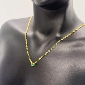 Close-up of a gold chain necklace with a round green gemstone on a black mannequin