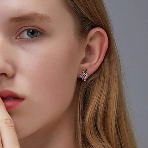 Detailed close-up of a delicate purple grape stud earring with a green leaf on the ear