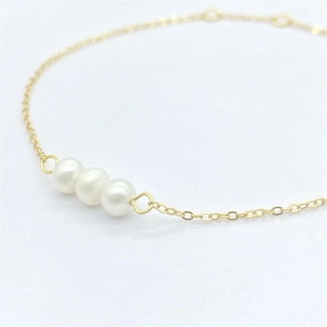 Elegant gold chain bracelet featuring three natural white pearls on a white background