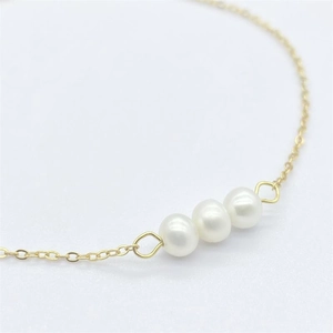 Macro detail of three lustrous white pearls on a minimalist gold chain bracelet