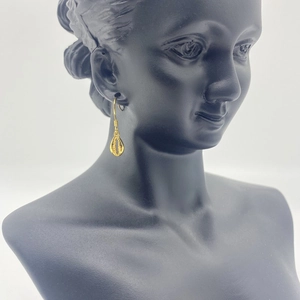 Macro side view of gold-plated shell pendant drop earrings on a minimalist black model