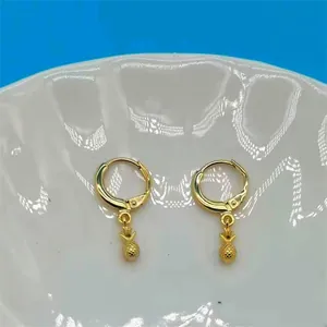 Detailed close-up of golden pineapple drop earrings on a white textured plate