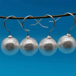 Detailed view of white pearl drop earrings with silver metal hooks on blue background