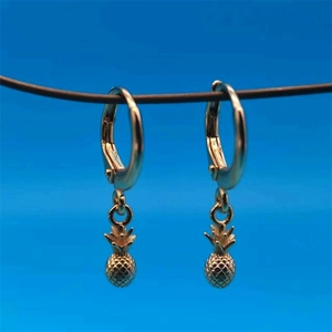 Close-up of golden pineapple pendant earrings with textured surface on blue background