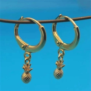 Detailed close-up of golden pineapple pendant earrings on light blue backdrop