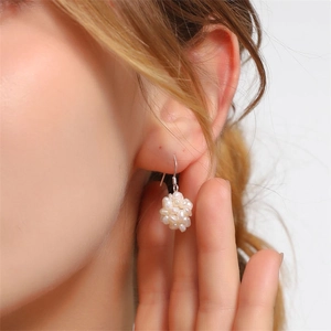 Detail of woven freshwater pearl cluster earrings worn by a model in a soft studio setting