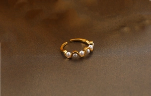 Detail view of wavy gold ring featuring five white pearls in a curve on textured dark surface