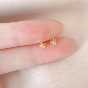 Close-up of mini gold heart stud earrings held by fingers to show delicate scale