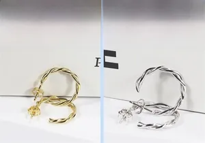 Dettaglio di orecchini a cerchio a fune intrecciata oro e argento su cartoncini bianchi