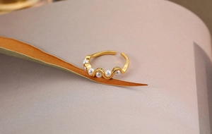 Macro detail of gold wave ring featuring five white pearls and adjustable open band