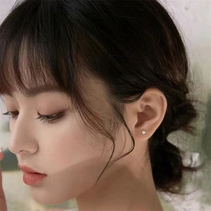 Close-up of minimalist silver heart stud earrings worn by a model to show actual size