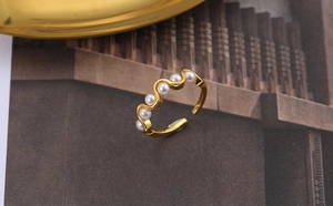 Macro detail of wave-shaped gold ring with five white pearls on a textured background