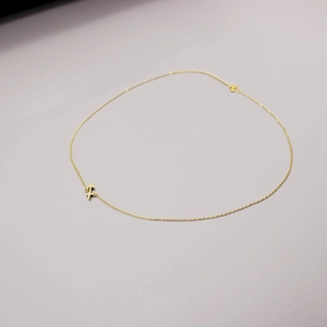 Detail of minimalist golden arrow pendant necklace with fine chain on grey background