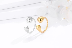 Close-up of gold and silver water drop rings on a minimalist white floral background