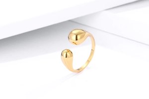 Close-up of polished gold teardrop open ring on a minimalist white geometric background