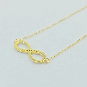 Dettaglio della collana con ciondolo infinito dorato e catena sottile su superficie