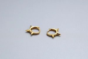 Close-up of gold punk rivet huggie earrings with sparkling crystals on grey background