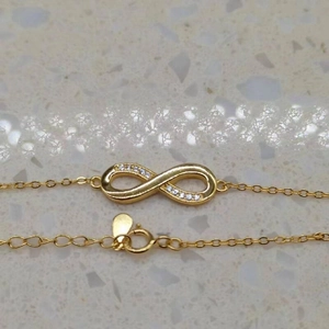 Close-up of golden infinity symbol bracelet with sparkling cubic zirconia on a stone surface