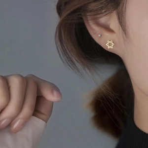 Close-up of a hollow hexagram gold stud earring and a tiny zircon stud on model ear