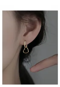 Detail view of a model wearing gold heart pendant earrings with rectangular hoops