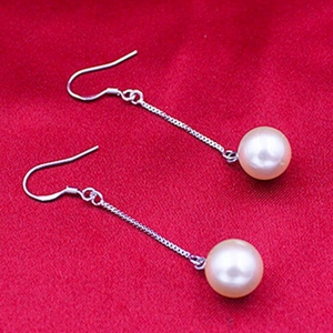Macro view of long s925 silver hook earrings with round white pearl drop on red fabric