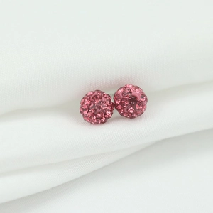 Close-up of pink crystal ball stud earrings on white silk fabric in macro view