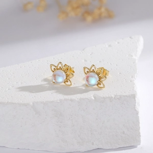 Asymmetric moonstone sunflower stud earrings in gold finish on a textured stone surface