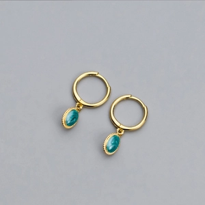 Close-up of vintage golden hoop earrings featuring oval green pendants with beaded edges