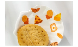 Macro shot of shell-shaped ceramic plate featuring colorful hand-drawn cartoon food patterns
