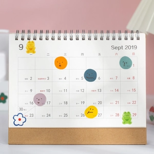 Cute cartoon bear and emoji stickers decorating a minimalist white spiral desk calendar