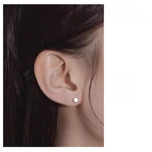 Detail of a minimalist gold hexagonal stud earring with polished mirror finish on model