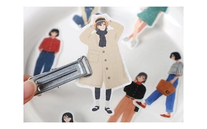 Close-up of artistic girl stickers in fashion outfits being held by a metal clip in a tray