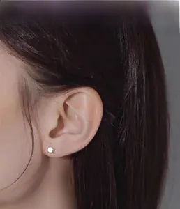 Close-up of a minimalist hexagonal gold stud earring worn on the earlobe with shiny finish