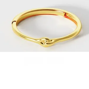 Macro detail of a minimalist knotted golden sterling silver bangle with a high-polished finish
