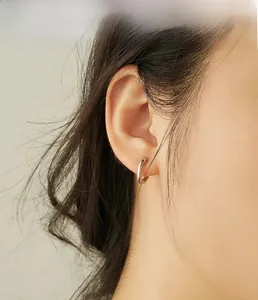 Gros plan de boucles d'oreilles créoles minimalistes en argent poli portées à l'oreille