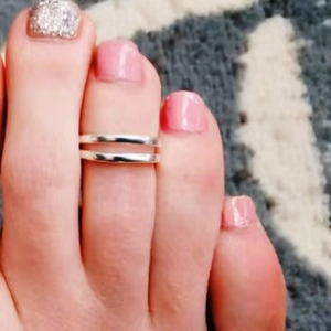 Détail d'une bague d'orteil argentée à double anneau sur un pied avec vernis rose