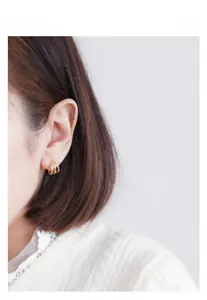 Gros plan d'un mannequin portant des boucles d'oreilles géométriques dorées à trois anneaux