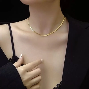 Minimalist gold flat snake bone necklace worn by a model against a black background