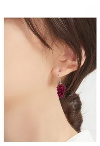 Detailed close-up of grape-shaped dark red bead earrings worn by a model in soft light