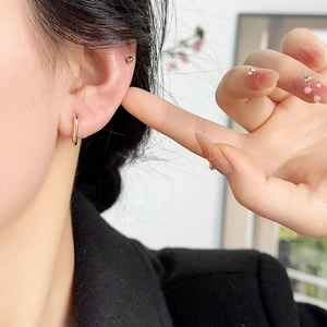 Minimalist gold U-shaped ear buckle and silver ball stud earrings worn by a model