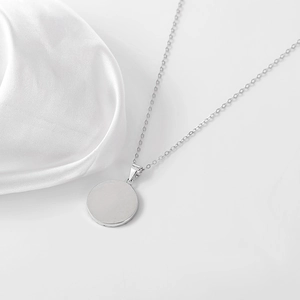 Dettaglio collana con ciondolo tondo in argento lucido su sfondo di seta bianca