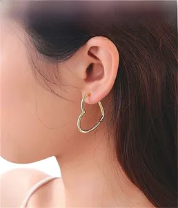 Side view of model wearing a large golden heart-shaped hoop earring in S925 silver