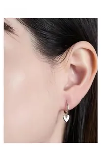 Close-up of 925 sterling silver heart charm hoop earrings worn on a female ear