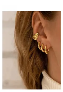 Detailed close-up of golden twisted hoop earrings and matching ear cuff on a model's ear