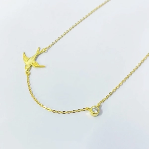 Détail macro du pendentif hirondelle dorée avec pierre scintillante sur chaîne fine