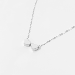 Macro shot of silver dual heart-shaped pendant on a minimalist fine cross chain